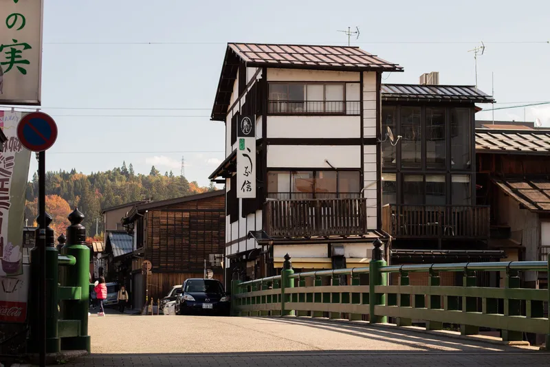Timber townhouses beside a green-railed bridge in Takayama on an autumn day