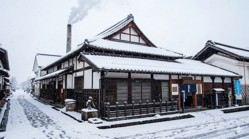 Snow-covered sake brewery with a smoking chimney on a quiet street in the Hida region