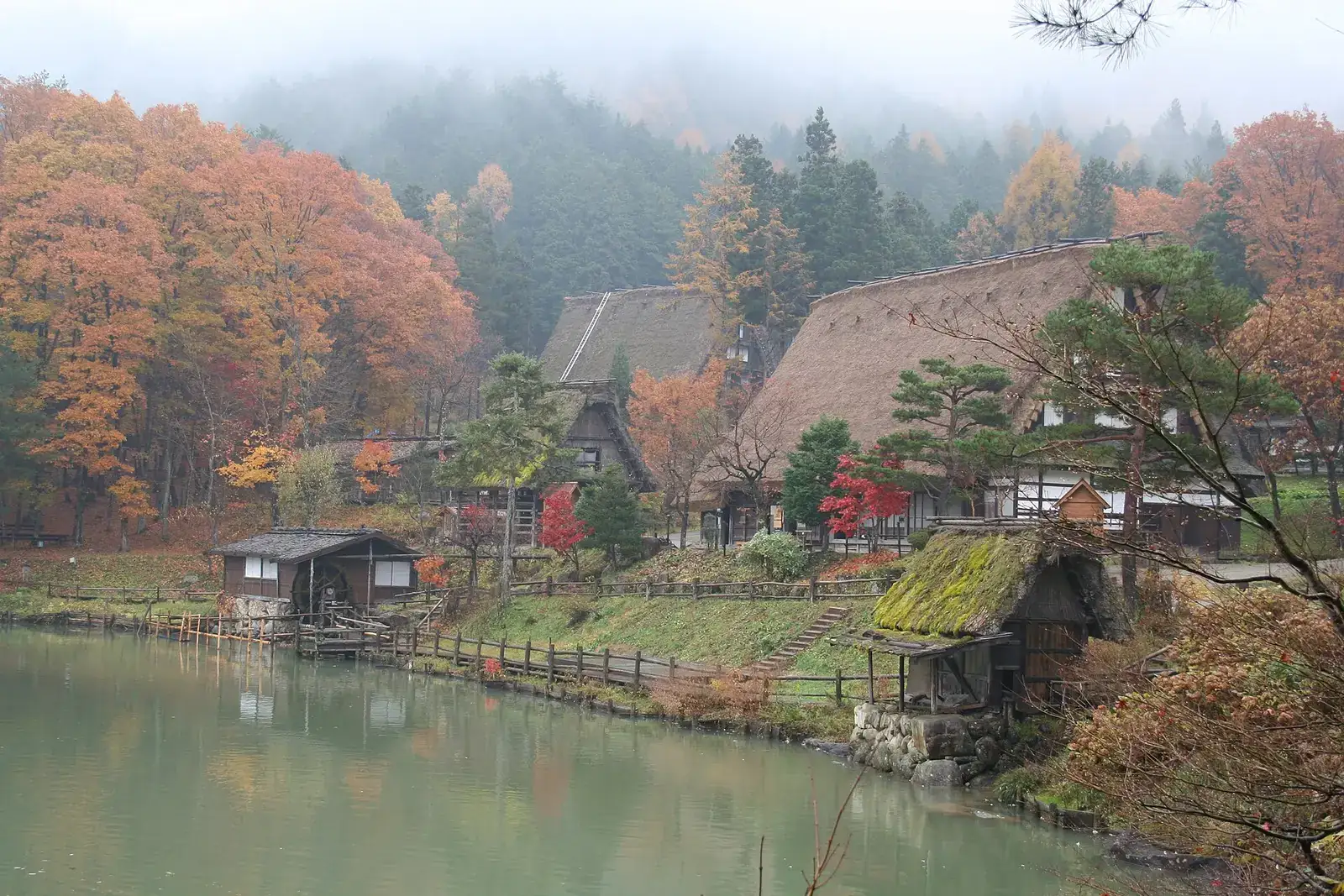 Thatched farmhouses and a water mill around the pond at Hida Folk Village in misty autumn colour