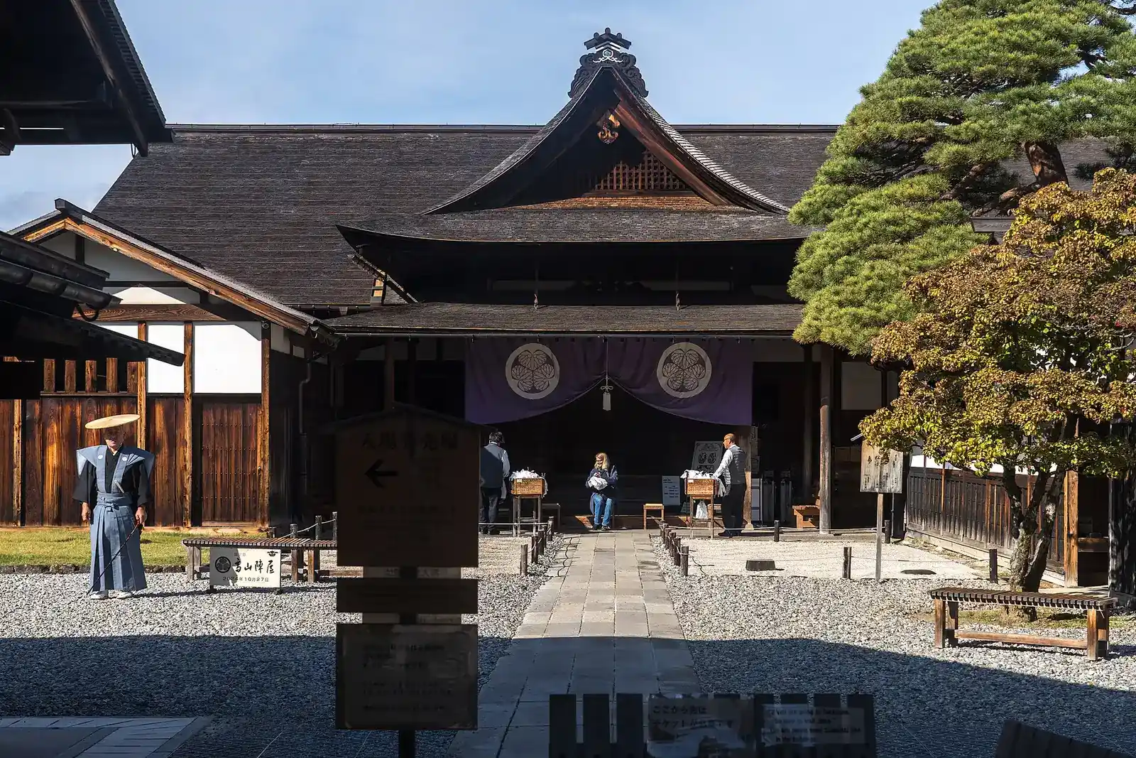 Main gate of Takayama Jinya with its purple crest curtain, a costumed guide in the courtyard