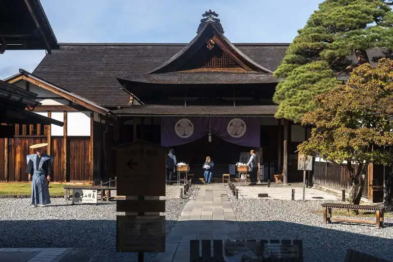 Main gate of Takayama Jinya with its purple crest curtain, a costumed guide in the courtyard