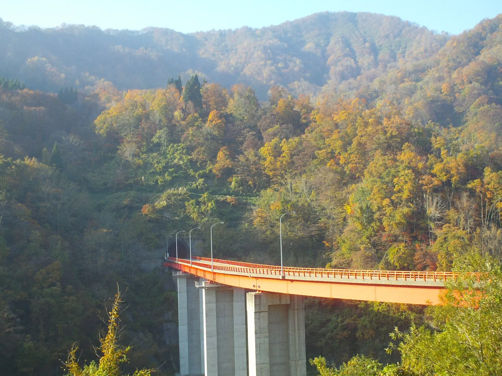 Orange road bridge on Route 304 crossing a wooded valley in autumn near Gokayama