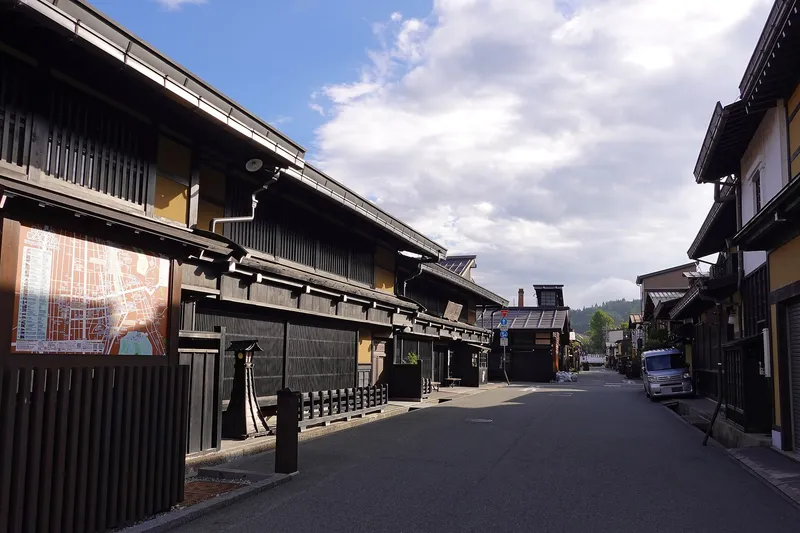 Wide view down a quiet Sanmachi street of dark timber houses under a blue sky