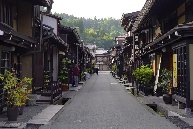 Sanmachi street with potted plants by the doors and green hills at the far end