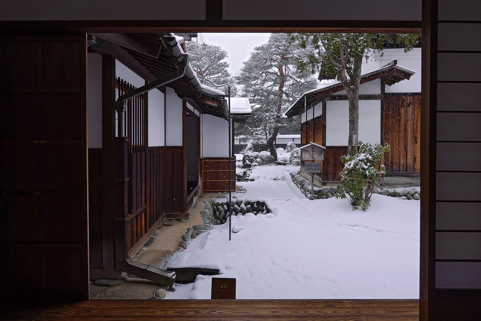 Snowy courtyard of Takayama Jinya framed by a dark wooden doorway