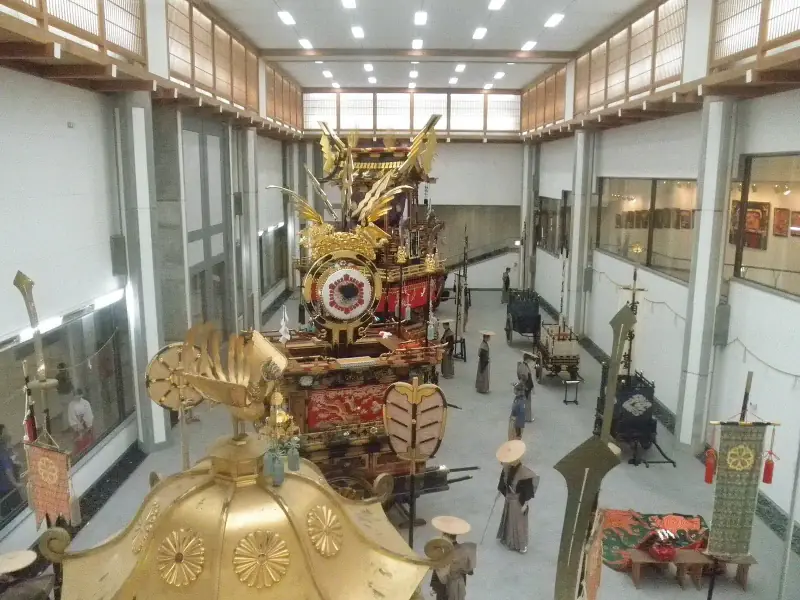 Looking down the Takayama Yatai Kaikan hall over a gilded mikoshi to a festival float with a phoenix top