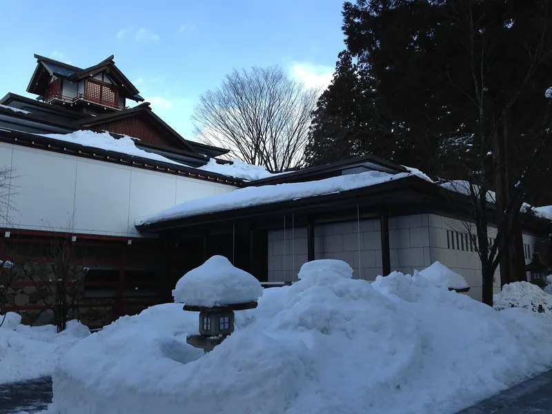 Takayama Yatai Kaikan exhibition hall in winter, snow piled on its roofs and stone lanterns