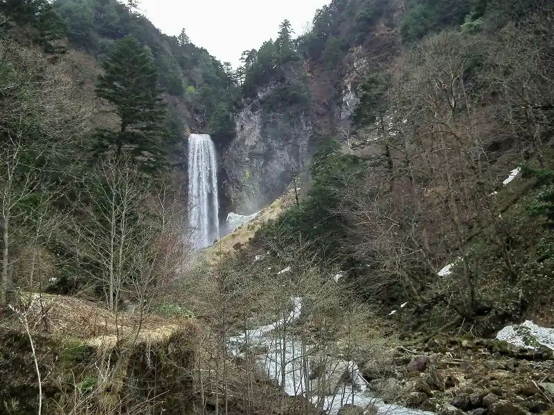 Wide view of Hirayu Falls in early spring, bare trees and late snow in the valley below