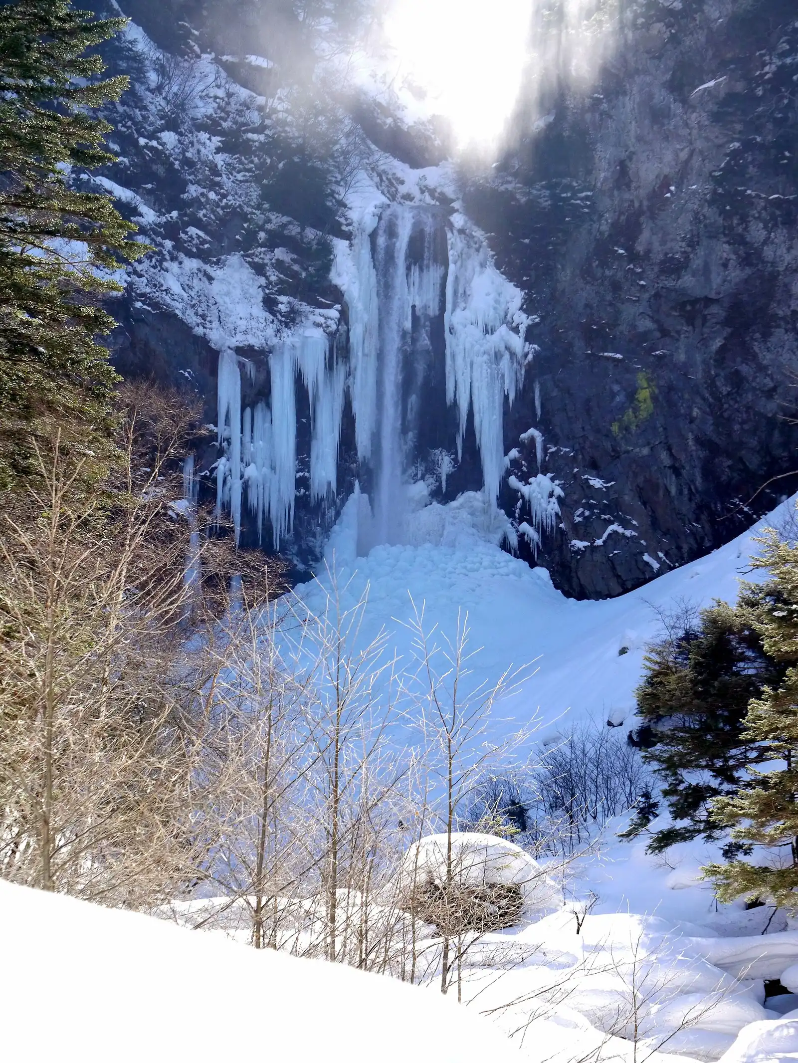 Hirayu Falls almost fully frozen in midwinter, sun breaking over the cliff top