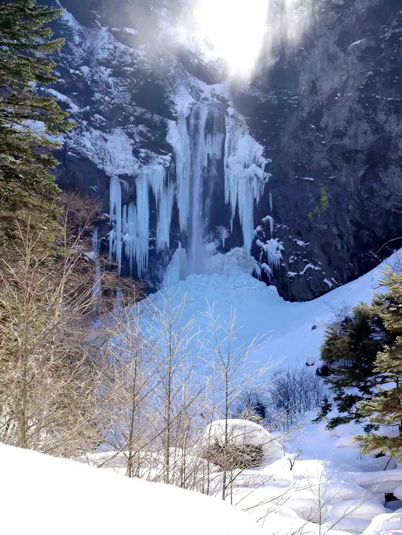 Hirayu Falls almost fully frozen in midwinter, sun breaking over the cliff top