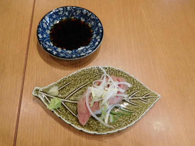 Slices of Hida beef nigiri sushi on a leaf-shaped plate with soy sauce