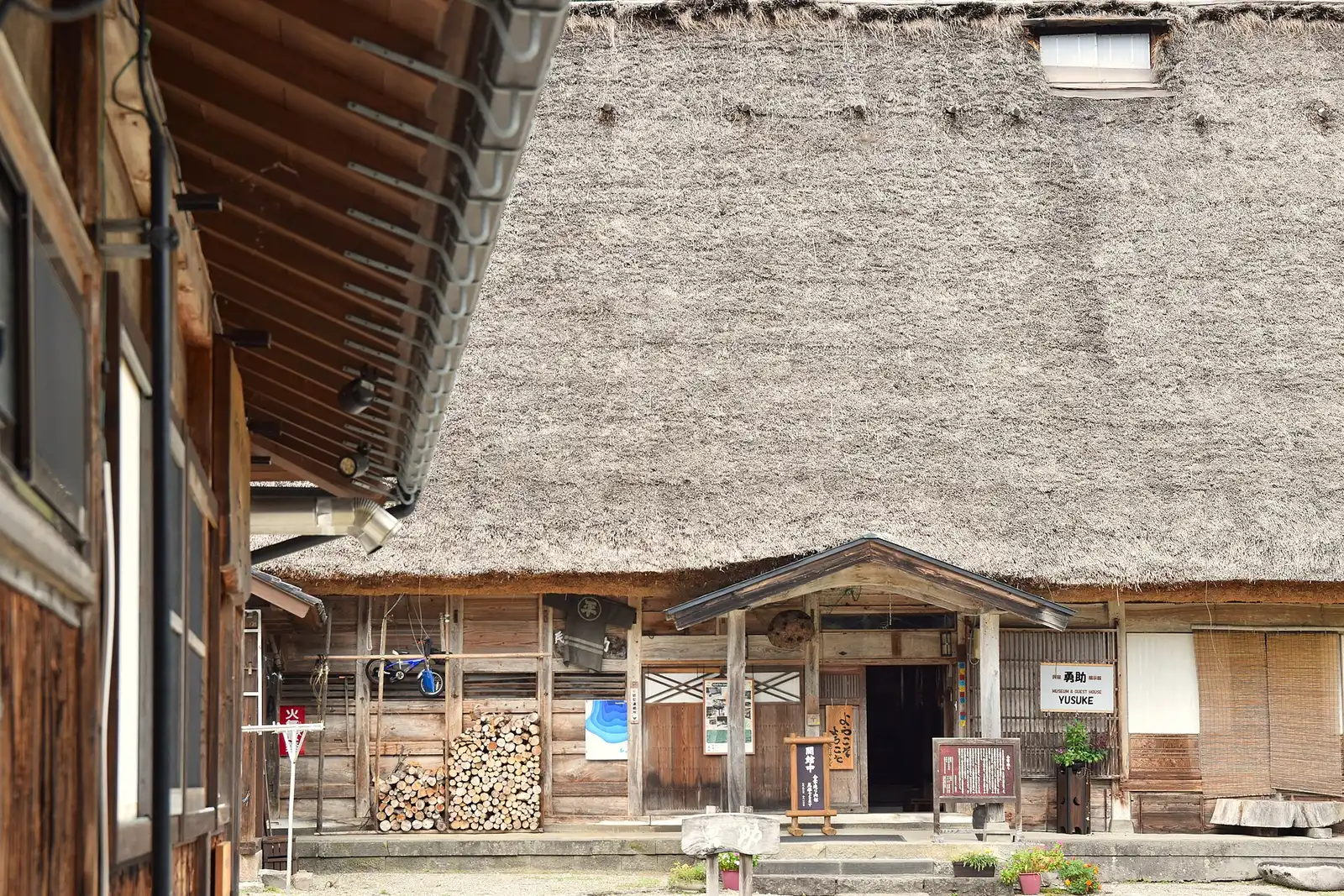 Thick thatch over a house entrance in Ainokura, firewood stacked by the door