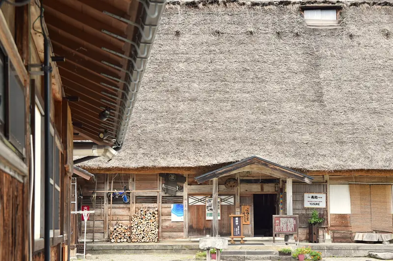 Thick thatch over a house entrance in Ainokura, firewood stacked by the door
