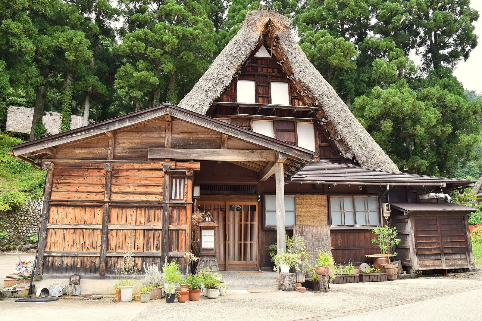 Front of a thatched gassho house in Ainokura with a wooden porch and potted plants